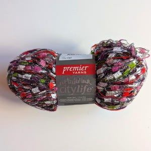 May include: A skein of Premier Yarns City Life yarn featuring a multi-colored, textured blend of black, silver, pink, red, and green fibers. A central paper label displays the brand name, the text City Life, and a lot number of 1187.