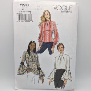 May include: Vogue Patterns V9285 sewing pattern envelope featuring three blouse designs. Design A is a floral print top with flared sleeves. Design B is a solid white blouse with bell sleeves. Design C is a red and white patterned top with long sleeves.