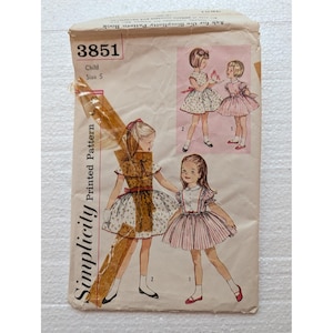 May include: A vintage Simplicity printed pattern envelope, number 3851, for a child's size 5 dress. The beige paper envelope features illustrations of two children wearing different dress styles, with a piece of clear adhesive tape across the front.