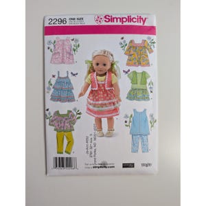 Puede incluir: Un sobre de patrón de costura Simplicity 2296 para ropa de muñeca. El frente muestra una muñeca con un vestido rosa de lunares, una blusa amarilla y cintas verdes. Las ilustraciones muestran varias combinaciones de vestidos, tops y pantalones.