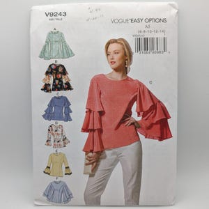 May include: Vogue Easy Options V9243 sewing pattern envelope featuring a model wearing a coral-colored long-sleeve top with tiered ruffled sleeves and white trousers. The envelope displays six variations of the top design labeled A through F.