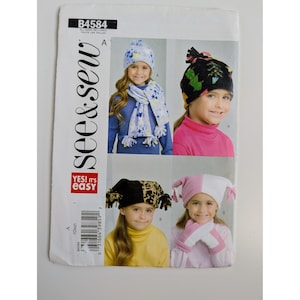 May include: A See & Sew B4584 sewing pattern envelope featuring illustrations of children wearing various fleece hats, scarves, and mittens. The designs include star patterns, a black hat with tree prints, a leopard print hat, and pink and white sets.