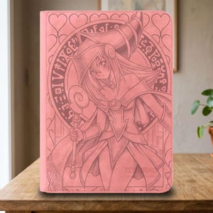 Puede incluir: Una funda protectora rectangular de color rosa con una ilustración grabada con láser de una maga de estilo anime sosteniendo un bastón. El diseño incluye un fondo circular con símbolos místicos y un borde con patrón de corazones.