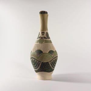 May include: A tall ceramic bottle with a narrow neck and a flared base, featuring a matte cream finish. The body is decorated with carved, layered patterns in shades of sage green, dark forest green, and black, showcasing geometric motifs.