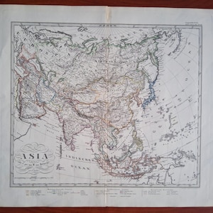 May include: An antique paper map of Asia featuring detailed geographical outlines, mountain ranges, and coastlines. The map includes the title ASIA in a decorative script, various regional labels in German, and a legend at the bottom.