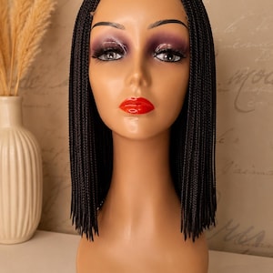 May include: A shoulder-length black braided wig with a centre part, displayed on a mannequin head. The wig features thin, uniform micro-braids that fall straight down, framing the face with a sleek, blunt-cut appearance at the ends.