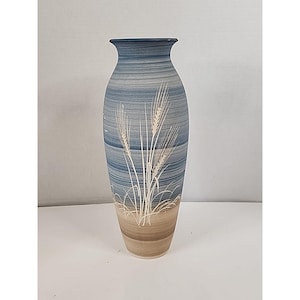 May include: A tall, slender ceramic vase featuring a gradient design that transitions from a light tan base to a blue-toned upper section. The surface is decorated with white, etched-style illustrations of wheat stalks and grasses.