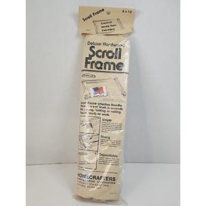 May include: A Deluxe Hardwood Scroll Frame in its original packaging, measuring 15.24 by 30.48 cm. The beige plastic packaging features black text, illustrations of the frame, and a small American flag sticker, labelled for cross-stitch and needlepoint.