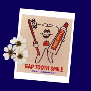 May include: A rectangular print featuring a cartoon tooth with a gap-toothed smile, holding a red toothbrush and a tube of The Crux toothpaste. A small red apple is centred on the tooth. Text reads GAP TOOTH SMILE and HOW LUCKY CAN A SIMPLE MAN BE?