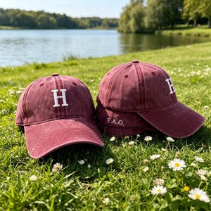 Puede incluir: Dos gorras de béisbol color granate con un acabado desgastado. Cada gorra presenta una letra H bordada en blanco en el panel frontal. Una gorra muestra el texto F.A.O. bordado en blanco en el panel lateral cerca de la visera.