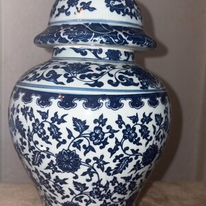 Puede incluir: Un tarro de jengibre de cerámica blanca con tapa extraíble, que presenta un detallado patrón floral azul. El diseño incluye intrincadas enredaderas, hojas y flores que cubren el cuerpo y la tapa, con un borde festoneado cerca del cuello.