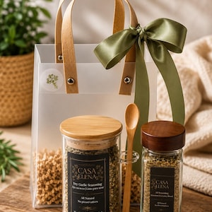 Peut inclure: Un sac cadeau transparent avec des anses en bois et un ruban vert olive, contenant un pot en verre d'assaisonnement à l'ail sec Casa Elena de 106 g, un pot d'assaisonnement complet Casa Elena de 99 g et une petite cuillère en bois.