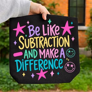 May include: A black fabric item featuring the colorful text "Be Like Subtraction AND MAKE A DIFFERENCE" in pink, yellow, purple, and teal. The design includes pink stars, teal and pink smiley faces with star eyes, and small diamond shapes.