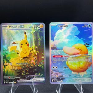 May include: Two holographic Pokémon trading cards displayed on clear plastic stands. The left card features Pikachu ex with 200 HP and the Thunderbolt attack. The right card features Psyduck with 70 HP, the Damp ability, and the Ram attack.