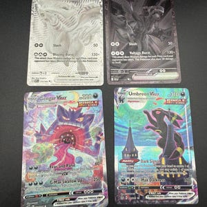 May include: Four collectible trading cards featuring Reshiram EX, Zekrom EX, Gengar VMAX, and Umbreon VMAX. The cards display detailed character illustrations, attack statistics, and game text, with holographic finishes on the Gengar and Umbreon cards.