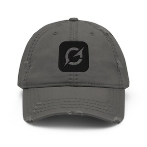 Peut inclure: Une casquette de baseball gris anthracite avec une finition usée et vieillie. Le panneau avant présente un écusson carré noir avec un logo en forme de flèche circulaire blanche. La casquette possède une visière courbée et des œillets.