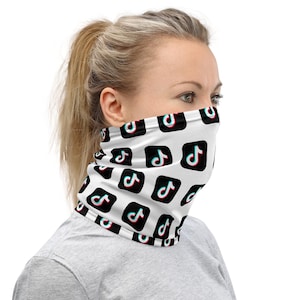 May include: A white neck gaiter featuring a repeating pattern of black square icons, each containing the cyan and magenta TikTok musical note logo. The fabric covers the lower face and neck, displaying multiple instances of the social media brand symbol.