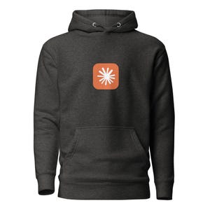 May include: A dark charcoal heather gray hooded sweatshirt featuring a front kangaroo pocket and a centered graphic of a white starburst icon set against a rounded square orange background on the chest area of the garment.