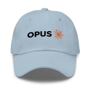 Op de afbeelding: Een lichtblauwe baseballpet met het woord OPUS in dikke zwarte hoofdletters, gevolgd door een gestileerde oranje zonnestraalgrafiek op het voorpaneel. De pet heeft een gebogen klep, een knoop aan de bovenkant en gestikte oogjes voor ventilatie.