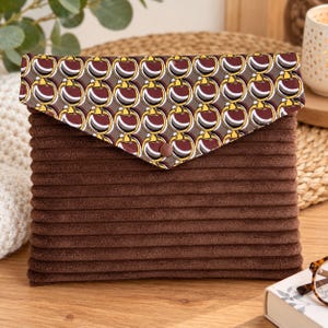 May include: A brown corduroy pouch featuring a triangular flap with a repeating pattern of gold, white, and dark red circular horse bit motifs. The pouch is secured with a single brown snap button centered on the flap.