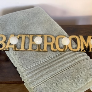Vintage wall mount brass BATHROOM sign features five hooks with white porcelain knobs. A great feature piece for any bathroom!