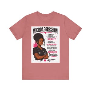 May include: A dusty rose t-shirt featuring a graphic of a person with dark skin and curly hair wearing a black scrub top and stethoscope. The text reads: MICROAGGRESSION A BRIEF, EVERYDAY SLIGHT, WHETHER INTENTIONAL, OR UNINTENTIONAL, THAT COMMUNICATES HOSTILE, DEROGATORY, OR NEGATIVE MESSAGES TO PEOPLE OF MARGINALIZED IDENTITIES.