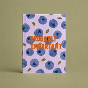 May include: A hardcover notebook with a light purple cover featuring a repeating pattern of dark blue blueberries and small green leaves. The text PROBABLY IMPORTANT is printed in bold orange capital letters across the center of the front cover.
