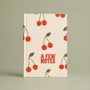 May include: A hardcover notebook with a cream-colored cover featuring a repeating pattern of red watercolor cherries with green leaves. The text A FEW NOTES is printed in bold red capital letters in the center of the front cover.