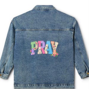 Könnte beinhalten: Eine blaue Jeansjacke mit dem Wort PRAY in großen, bunten, gemusterten Blockbuchstaben auf der Rückseite. Jeder Buchstabe ist mit verschiedenen Designs verziert, darunter Vichy-Karos, Punkte und Blumenmuster in Rosa-, Blau- und Grüntönen.