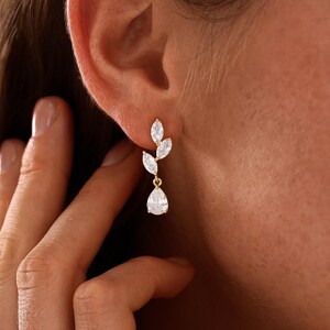 May include: A gold-toned drop earring featuring three marquise-cut clear stones arranged in a vertical leaf-like pattern, terminating in a single pear-shaped clear stone pendant. The earring is secured to the earlobe with a small gold-toned post.