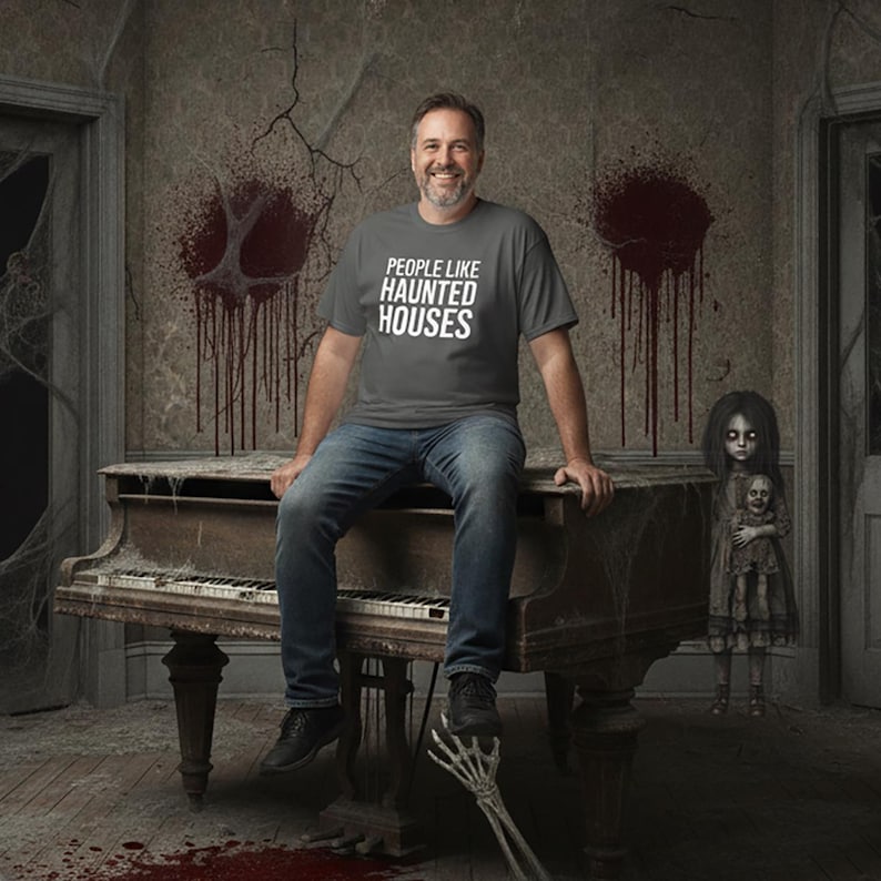 Peut inclure: Un t-shirt gris anthracite &agrave; manches courtes avec le texte blanc "PEOPLE LIKE HAUNTED HOUSES" imprim&eacute; sur la poitrine. Le v&ecirc;tement est port&eacute; avec un jean bleu et des chaussures noires, pr&eacute;sentant une coupe d&eacute;contract&eacute;e avec un col rond.