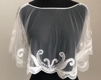 Può includere: Cappotto da sposa in pizzo bianco trasparente con ricami di perline. Il mantello ha un bordo a festoni e un delicato motivo floreale.