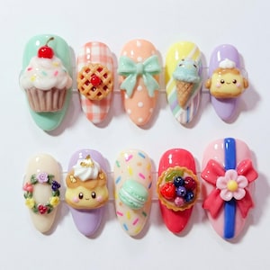 May include: A set of ten press-on nails featuring 3D charms including a cupcake, cherry pie, mint bow, ice cream cone, smiling pastry, floral wreath, macaron, fruit tart, and a pink bow with a flower, all in pastel and vibrant colors.