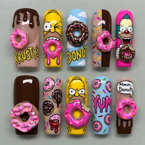 May include: A set of ten press-on nails featuring colorful designs inspired by The Simpsons, including illustrations of Homer Simpson and Krusty the Clown, various donut graphics, and 3D-style donut embellishments with text like Krusty's, Donuts, Yum, and Mmm... Donuts.