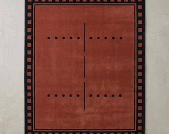 Puede incluir: Una alfombra rectangular con un centro de color rojo terracota intenso y un borde negro compuesto por un patrón de cuadrados repetitivos. El campo interior muestra una línea vertical negra central cruzada por dos filas horizontales de puntos negros.