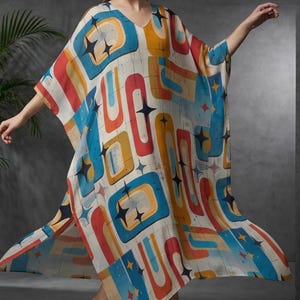 May include: A flowing, V-neck caftan in a retro-inspired print. The caftan features a white background with colorful geometric shapes in blue, orange, yellow, and red, accented with black starbursts. The model is wearing black heels.