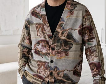 May include: A long-sleeve V-neck cardigan featuring an all-over print of Michelangelo's The Creation of Adam. The garment has a button-down front closure with dark buttons, ribbed cuffs, and a ribbed hem, worn over a solid black t-shirt.