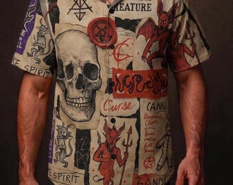 May include: Short-sleeved shirt with a beige background and a collage of illustrations. The shirt features a skull, devils, pentagrams, and text fragments. The overall design has a vintage, occult theme.