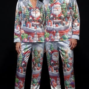Può includere: Completi pigiama a due pezzi in raso azzurro con stampa natalizia ripetuta. Il design include illustrazioni di Babbo Natale, renne, pupazzi di neve, alberi di pino e regali incartati. Ogni set presenta una camicia abbottonata con colletto e maniche lunghe, abbinata a pantaloni lunghi coordinati.