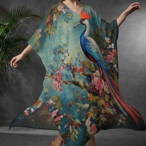 Puede incluir: Un caftán fluido de color turquesa con cuello en V, adornado con un pavo real vibrante y un diseño floral. El pavo real presenta tonos azules, rojos y naranjas, sobre un fondo de ramas florecientes. La prenda es ligera y parece ser de seda.