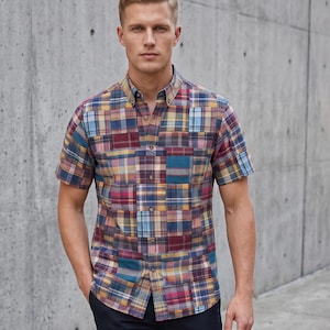 Pode incluir: Uma camisa de manga curta com botões, apresentando um padrão xadrez patchwork multicolorido em tons de azul, amarelo, vermelho e castanho. A camisa tem um colarinho clássico, uma carcela de botões frontal e uma bainha reta, combinada com calças azul-marinho.