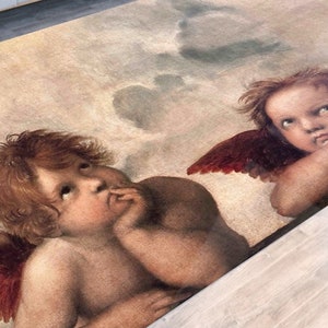 Puede incluir: Una alfombra rectangular con una pintura de estilo renacentista de dos querubines con alas rojas sobre un fondo nublado. La alfombra tiene una paleta de colores beige y marrón, con los querubines en primer plano.