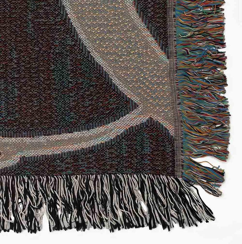 May include: A woven throw blanket with a geometric pattern in shades of brown, beige, and black. The blanket has a fringe border.