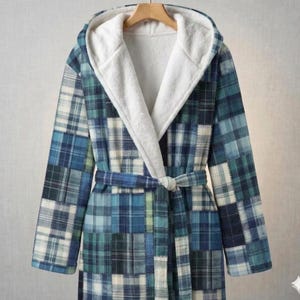 May include: A hooded robe with a patchwork plaid design in shades of blue, green, and white. The robe features a white, plush interior lining and a matching belt. The robe is hanging on a wooden hanger.