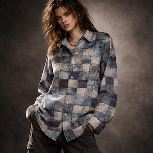 May include: A long-sleeved button-down shirt with a patchwork design in shades of blue, gray, and beige. The shirt has a classic collar and a single chest pocket. The fabric appears to be a soft, woven material. The shirt is paired with dark cargo pants.