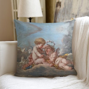 Puede incluir: Una almohada de tiro con una pintura vintage de dos querubines, uno colocando una corona de flores en la cabeza del otro. Los querubines están representados en una paleta de colores suaves y pastel sobre un fondo de cielo azul.