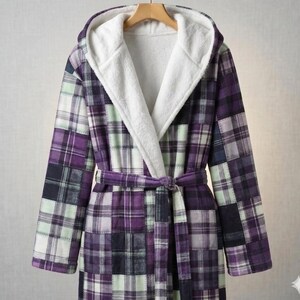 Peut inclure: Peignoir à capuche avec un motif patchwork à carreaux dans les tons de violet, blanc et vert. Le peignoir a une doublure intérieure en peluche blanche et une ceinture assortie. Il est suspendu à un cintre en bois.