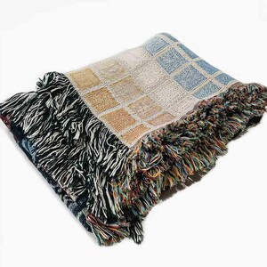 May include: A woven throw blanket with a colorful geometric pattern and fringe edging. The blanket is made of soft, textured yarn and features a mix of blue, yellow, and white colors.
