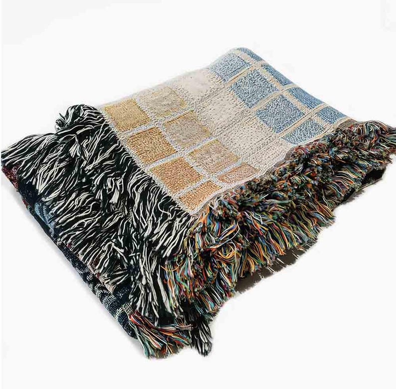 May include: A woven throw blanket with a colorful geometric pattern and fringe edging. The blanket is made of soft, textured yarn and features a mix of blue, yellow, and white colors.