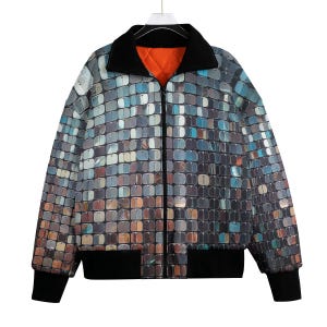 Può includere: Giacca con zip integrale con un motivo a mosaico nei toni del grigio, blu e marrone. Presenta colletto, polsini e orlo neri e una fodera trapuntata arancione. La giacca è appesa a un gancio.